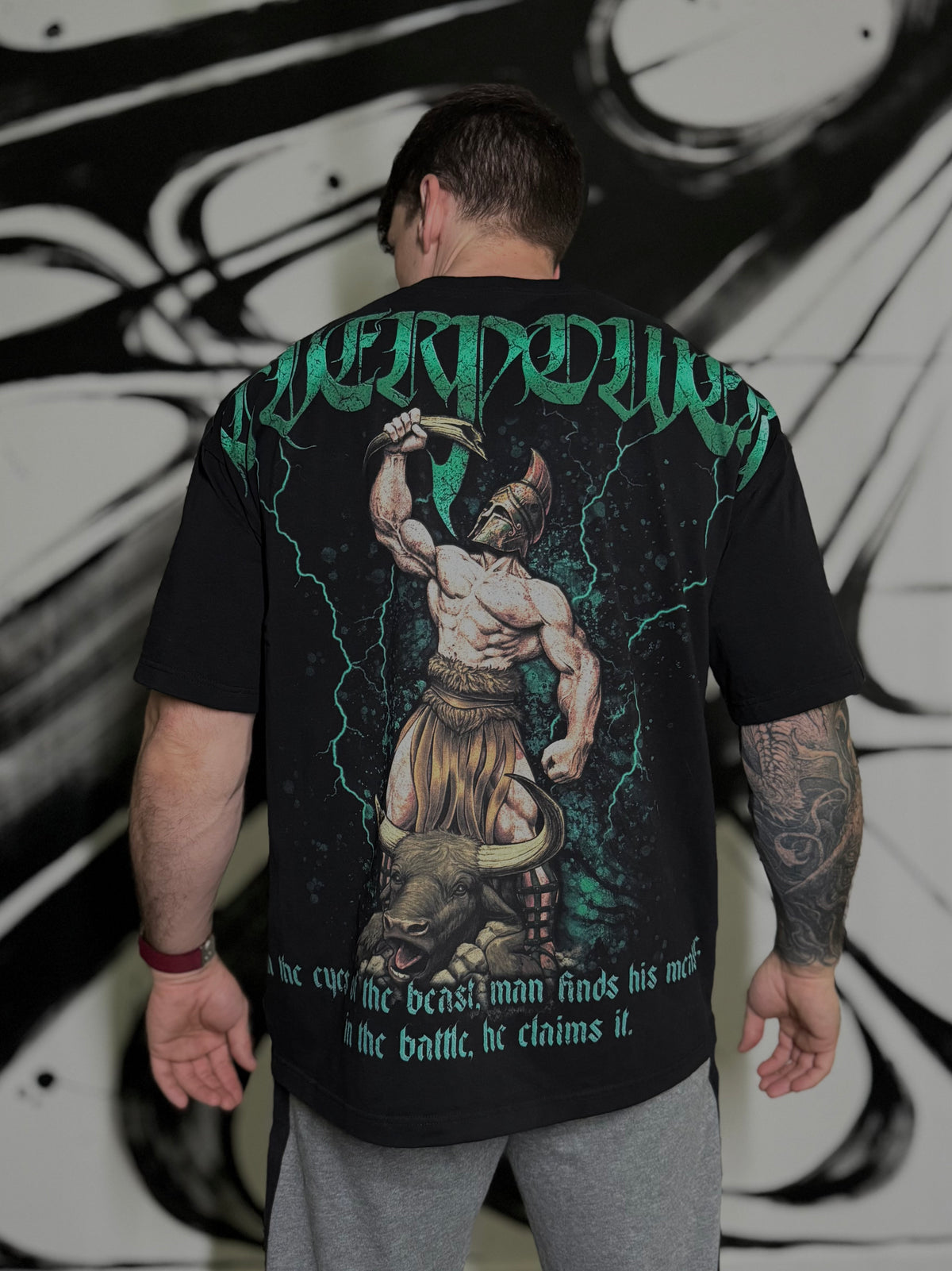 OverPower Strength Wear black oversized t-shirt worn, back view: Hercules raising the broken horn above a bull, green lightning, gothic OverPower lettering
