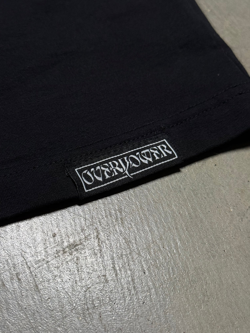 OverPower woven label sewn on the hem of the oversized tee