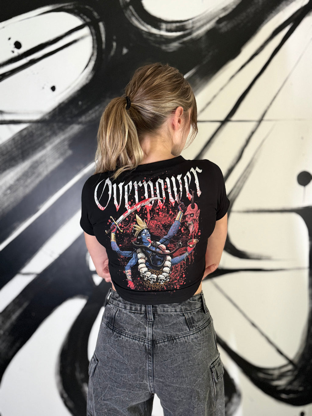 OverPower Strength Wear black crop tee worn, back view: Kali with blue skin and a raised sword on a red background, white gothic OverPower lettering